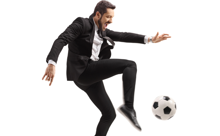 Homem de terno chutando bola de futebol