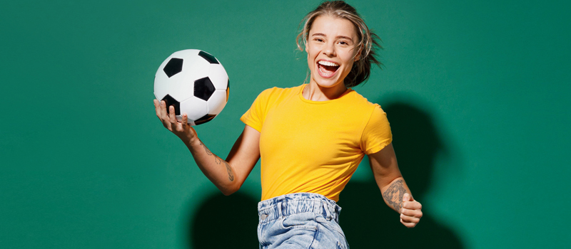 Mulher sorrindo com bola de futebol na mão